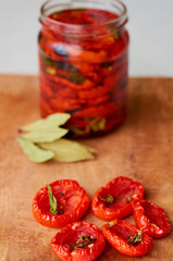 Dried red tomatoes with spices on wooden board close up. Jar with many dried tomatoes on the blurred background