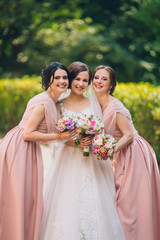Bride and bridesmaid in nature with bouquets of flowers. Funny wedding moments, bride show bridesmaids her new ring. Girls in shock.