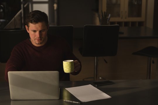 Disabled man having coffee while using laptop on dinning table