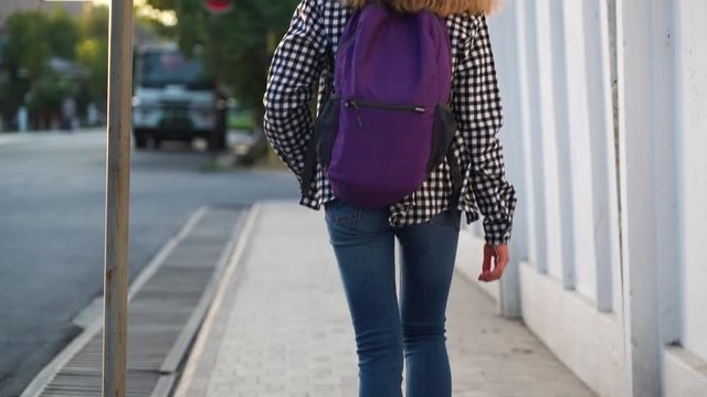 Girl is walking to school on the sidewalk in white sneakers with a purple backpack . Close-up of feet. Slow motion video.
