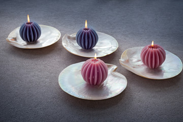 Four ribbed candles on pearl shells on concrete background.