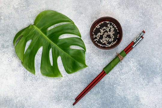 Asian food concept.  soy sauce with white sesame and Chopstick on a gray concrete surface with tropical leaves