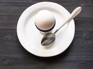 egg in cup and spoon on white plate on dark table