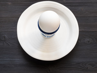 egg in cup on white plate on dark wooden table