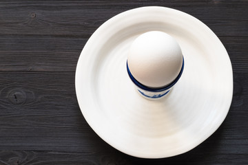 white egg in cup on plate on dark wooden table