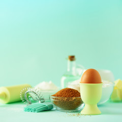 Bakery food frame, cooking concept. Different baking ingredients - butter, sugar, flour, milk, eggs, oil, spoon, rolling pin, brush, whisk over blue background. Copy space. Square crop