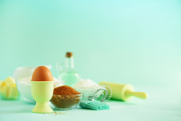 Healthy baking ingredients - butter, sugar, flour, eggs, oil, spoon, rolling pin, brush, whisk, milk over blue background. Bakery food frame, cooking concept. Copy space.