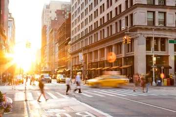  Drukke kruising van 23rd Street en 5th Avenue in Manhattan is vol met mensen en verkeer terwijl de zon op de achtergrond ondergaat. © deberarr