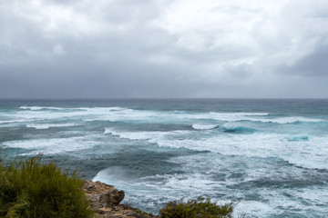 Fototapeta na wymiar Waves crashing on the rocky coastline with dark ominous storm clouds building on the horizon