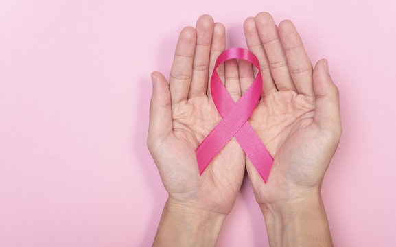 women hand holding pink ribbon breast cancer on pink background. with copy space