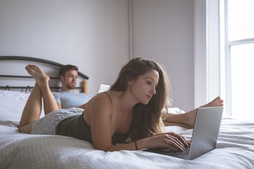 Couple using laptop and digital tablet in bedroom