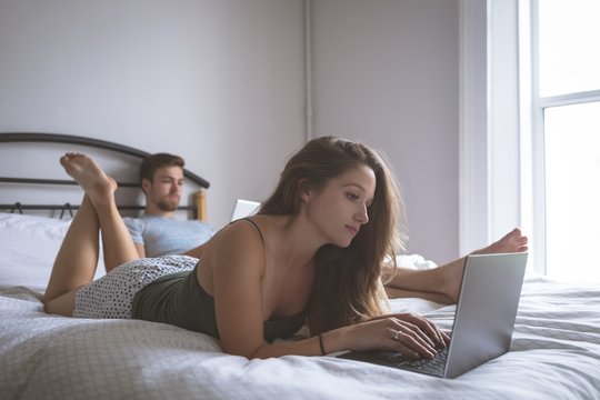Couple using laptop and digital tablet in bedroom - Powered by Adobe