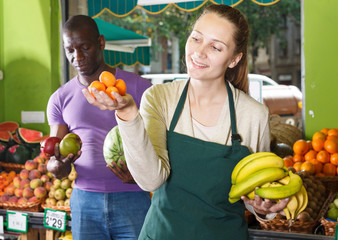 Obraz premium Smiling female seller is helping male client choose fresh fruits