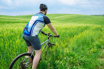 young strong man riding bicycle by green field