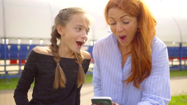 Two funny girl reacting to funny internet videos sitting outdoor in summertime.