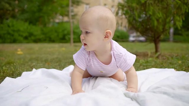 Close-up of a cute baby on white blanket in park meadow.