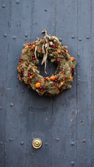Vintage Christmas wreath with cinnamon sticks, dry oranges, red balls and stars on the grungy wooden door. 