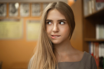 Pretty young student schoolgirl lady with long hair standing in empty classroom looking aside at copyspace bite her lip.