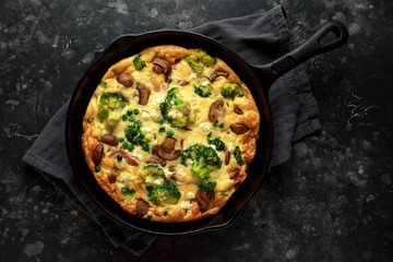 Homemade Frittata with mushrooms, broccoli, feta cheese, green peas and bacon on cast iron skillet