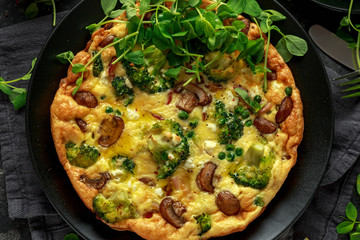 Homemade Frittata with mushrooms, broccoli, feta cheese, green peas and bacon on black plate