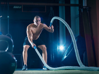 Fototapeta na wymiar Young man working out with battle ropes. Sports exercise in the fitness gym.