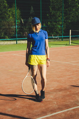 Portrait of a blonde girl with a short haircut. Background tennis court. Dark blue t-shirt polo and yellow shorts.Sport shooting.