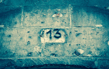 Black metal number 13 (indicating a house number) on the on the stone wall. Toned photo.