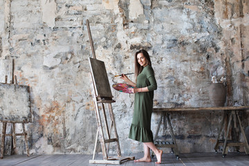 Woman in a green dress painting in an art studio and smiling.