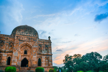Fototapeta na wymiar Stone dome at lodhi garden in delhi on a sunset evening with colorful clouds in pink, blue and white. This park filled with Mughal architecture is a popular spot for locals and tourists