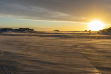 sunset on beach showing a wooden path leading to beach houses