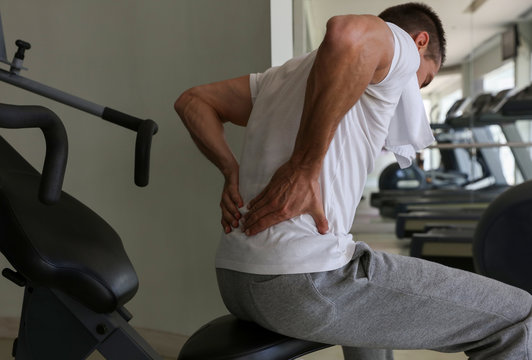 Man with suffering back pain in gym. Sports exercising injury