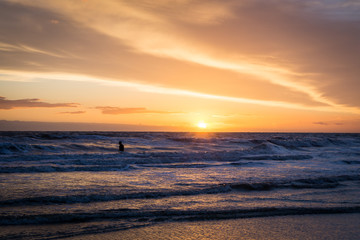 silhouette of a surfer standing in water at the beach during sunset