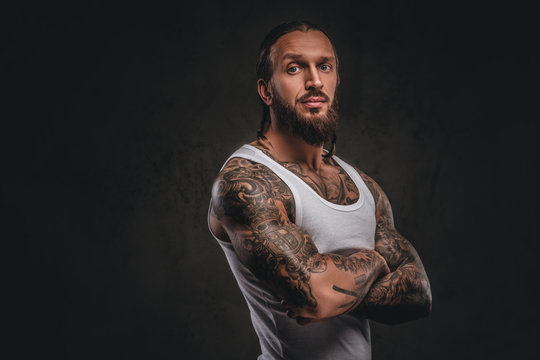 Brutal bearded tattooed male in white shirt posing with crossed arms. Isolated on a dark textured background.
