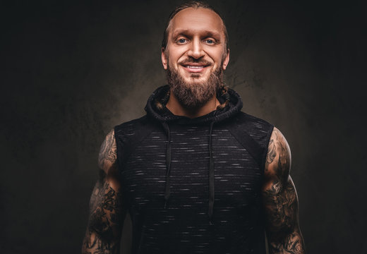 Portrait of a bearded tattooed athlete in a black hoodie. Isolated on a dark textured background.