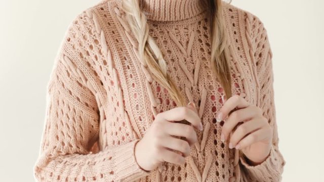 unrecognizable childish girl fiddling with her braids. woman in a knitted beige sweater holding her hair. idleness carefreeness