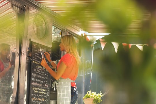 Female waitress writing menu on menu board while using digital
