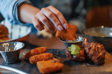 Close up of woman hands holding fried cheese and dipping it into a sauce.