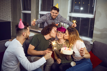Friends with cake with candles celebrating birthday at a party in room.