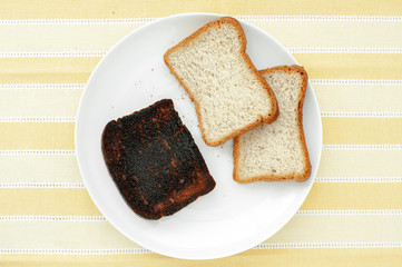 Slices of bread with one piece of burnt toast on striped yellow background.
