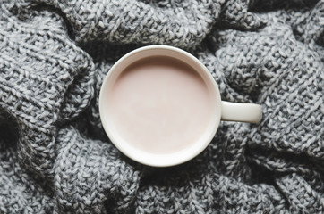 Obraz na płótnie Canvas A cup of hot cocoa with milk on gray wool knitted plaid. Home cosiness. Top view