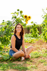 Young woman sitting laughing under a sunflower in the sunlight