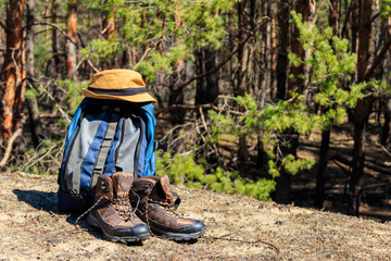 Tourist backpack, hiking boots and hat on the glade in pine forest