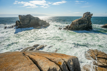 deux rochers en îlots,  face à face avec des vagues et de l'écume sous un ciel bleu