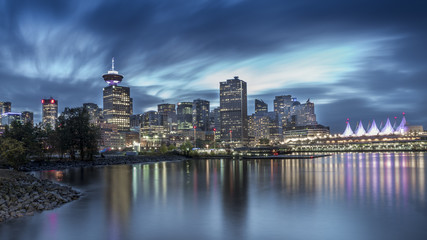 Fototapeta na wymiar Long exposure of Downtown Vancouver on a dramatic sky after a rain. Beautiful city mirroring in the pacific shore. British Columbia, Canada.
