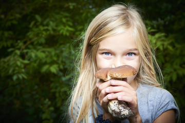 Child blong girl posing in forest and holding fresh picked mushroom (boletus). Selective focus