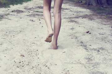 Fototapeta na wymiar Child girl bare feet walking along the forest sandy path. 