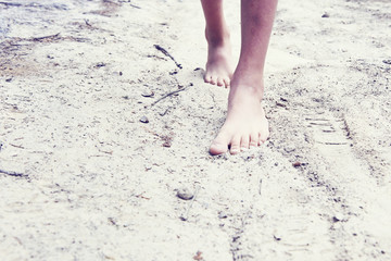 Child girl bare feet walking along the forest sandy path. 