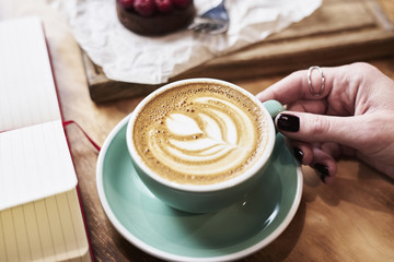 CLose-up cup of coffee latte on wooden table in woman hands from above. Having lunch in cafe.