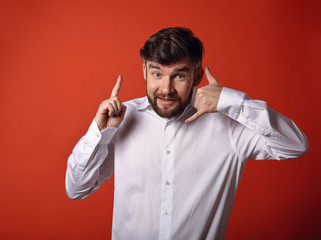 Smiling excited beard business man showing call me gesture and point up by the finger on bright red background. Closeup portrait with empty copy space