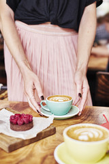 Cup of coffee latte and sweet pastry on wooden table in woman hands. Gentle romantic mood, girl wearing pink skirt